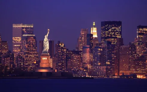 Statue of Liberty with New York City skyline at dusk, featured in self-guided walking tour app.