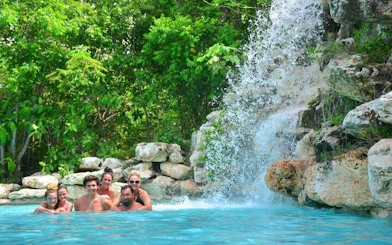 Visitors enjoying a waterfall pool in Punta Cana surrounded by lush greenery.