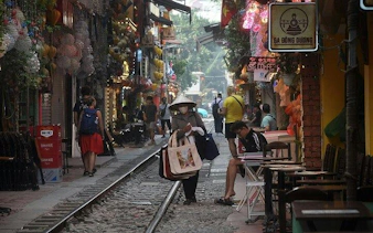 Hanoi street with train tracks, people walking, and colorful shops.