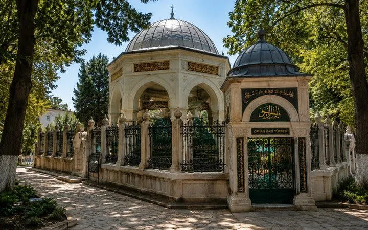 Orhan Gazi Tomb in Bursa surrounded by trees and ornate iron fencing.