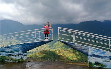 Person standing on Sa Pa glass bridge with scenic mountain view in background.