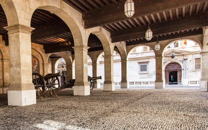 Historic Geneva arcade with cobblestone floor and cannons, part of self-guided city exploration game.