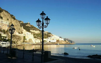 Seaside view of Amalfi coast with historic buildings and street lamps along the promenade.