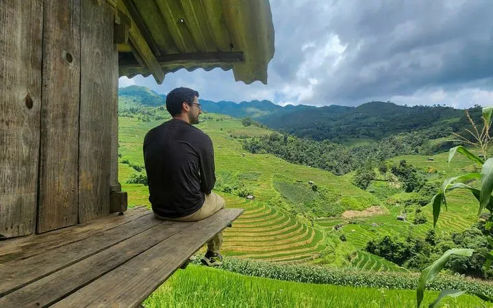 Man sitting on wooden porch overlooking terraced rice fields in Mu Cang Chai, Vietnam.