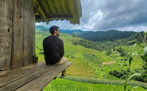 Man sitting on wooden porch overlooking terraced rice fields in Mu Cang Chai, Vietnam.