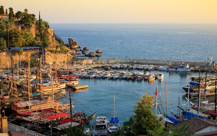 Antalya harbor with boats and cliffs during sunset on self-guided walking tour.