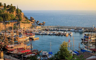 Antalya harbor with boats and cliffs during sunset on self-guided walking tour.