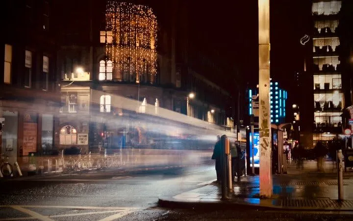 Night street scene in Glasgow with blurred lights and buildings, part of the Ghosts of Glasgow exploration game.