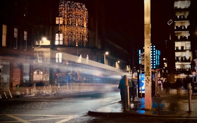 Night street scene in Glasgow with blurred lights and buildings, part of the Ghosts of Glasgow exploration game.