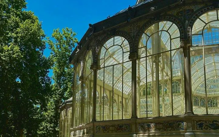 Glass pavilion at Real Jardín Botánico, Madrid, surrounded by trees under a clear blue sky.