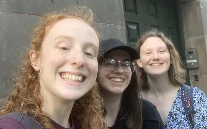 Three people smiling in front of a historic building in Manchester during a self-guided city exploration game.