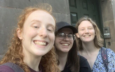 Three people smiling in front of a historic building in Manchester during a self-guided city exploration game.