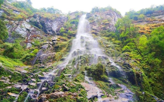 Waterfall cascading down rocky cliff surrounded by lush greenery in Sapa, Vietnam.