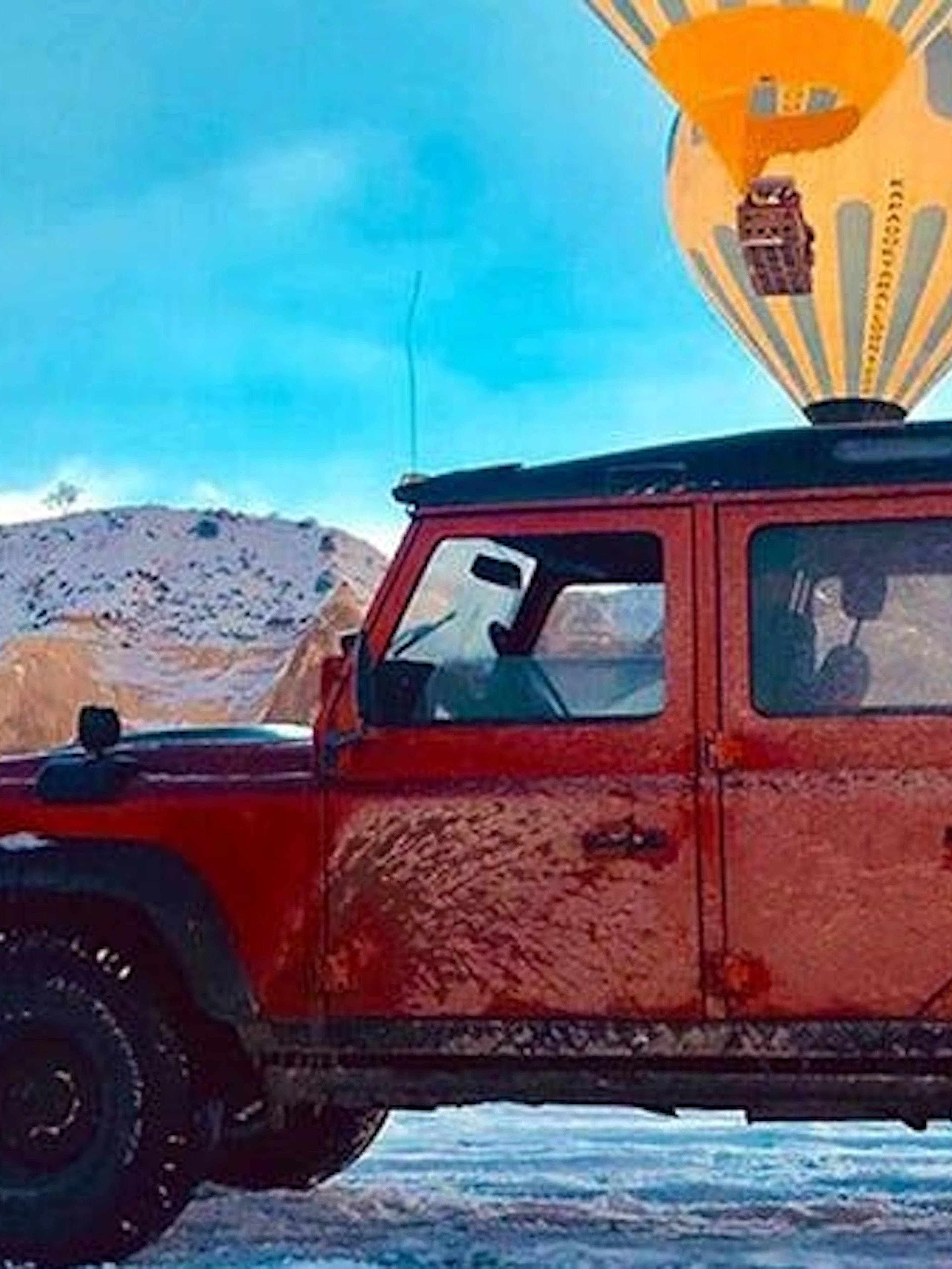 Jeep on snowy terrain with hot air balloon in Cappadocia.