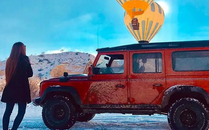 Jeep on snowy terrain with hot air balloon in Cappadocia.