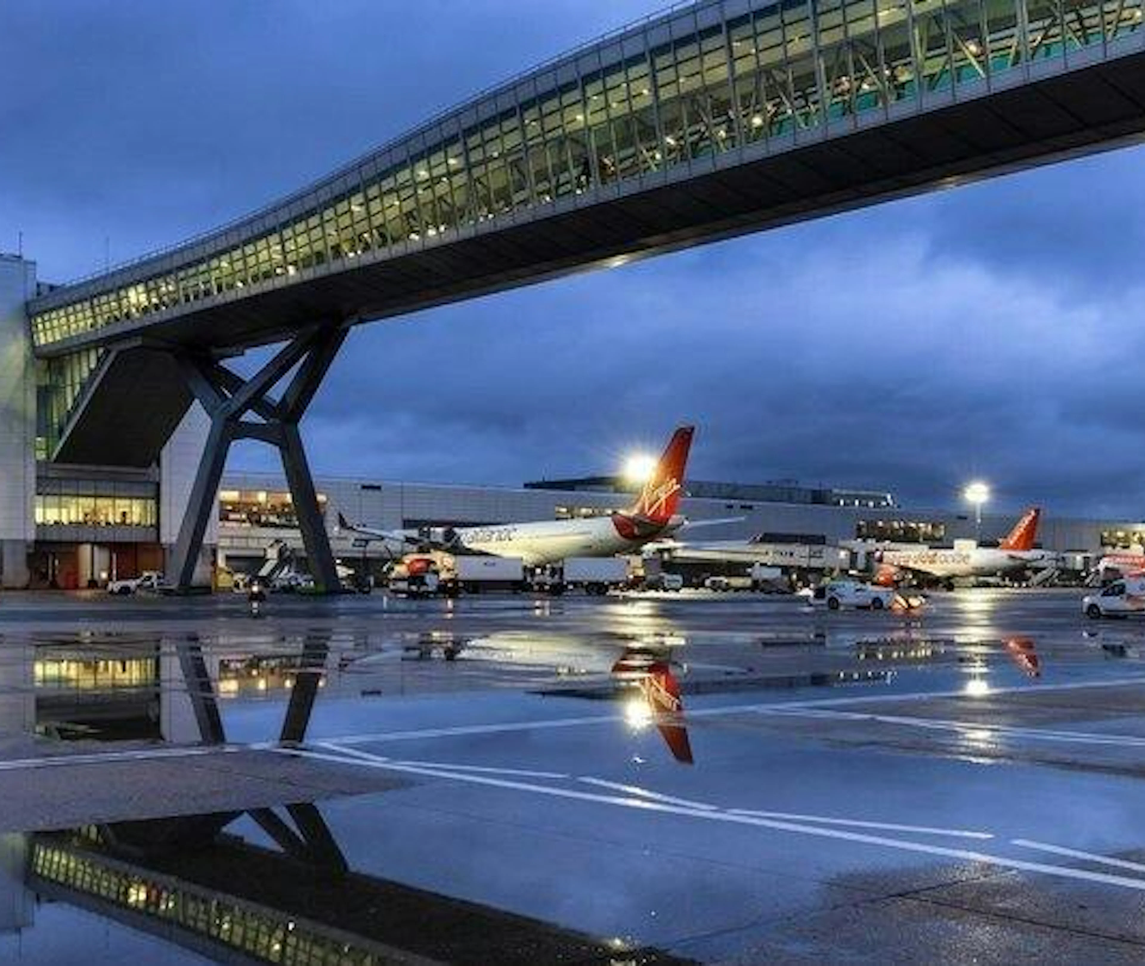 Gatwick Airport runway with planes and terminal bridge at dusk, London transfer service.