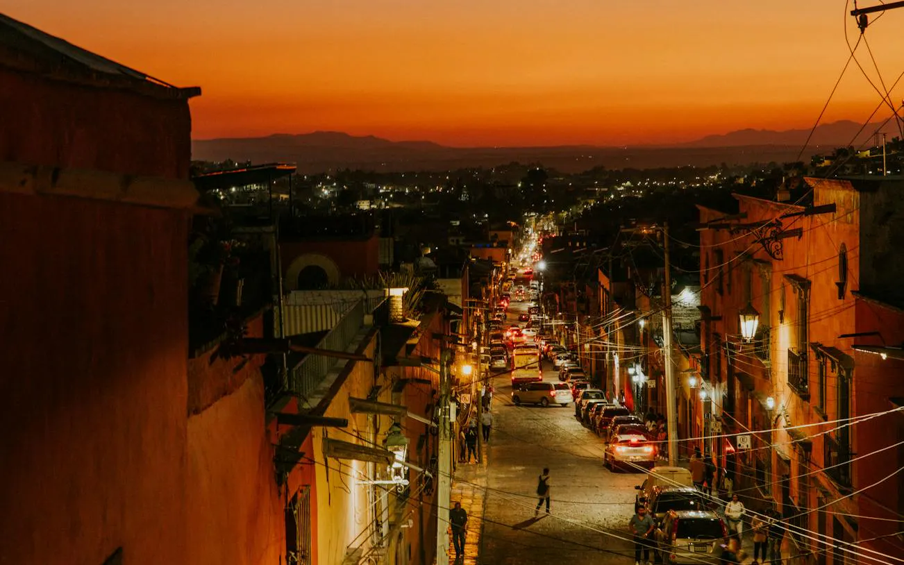 San Miguel de Allende street at sunset with vibrant lights and distant mountains.
