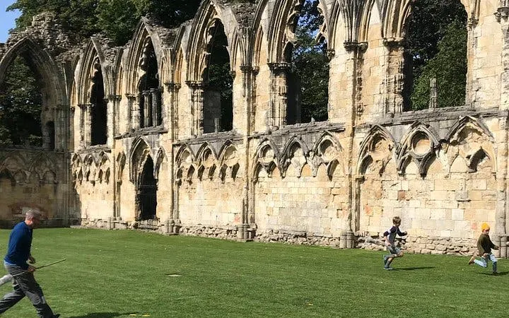 Ruins of St. Mary's Abbey in York with people playing on the grass during a Harry Potter walking tour.