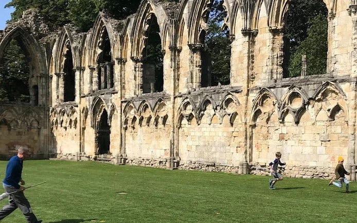 Ruins of St. Mary's Abbey in York with people playing on the grass during a Harry Potter walking tour.