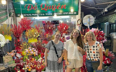 Women standing in front of a vibrant flower shop in a Ho Chi Minh City alley during a motorbike street food tour.