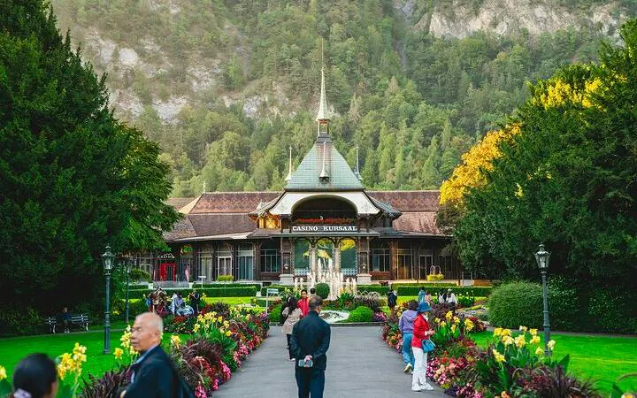 Casino Kursaal in Interlaken with visitors, surrounded by gardens and mountains, Bernese Oberland day trip.