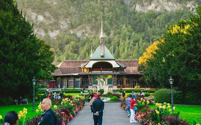 Casino Kursaal in Interlaken with visitors, surrounded by gardens and mountains, Bernese Oberland day trip.