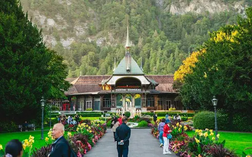 Casino Kursaal in Interlaken with visitors, surrounded by gardens and mountains, Bernese Oberland day trip.