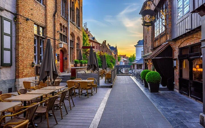 Romantic Bruges street with outdoor café seating and canal view at sunset.