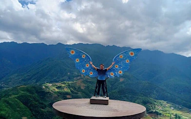 Person posing with butterfly wings at scenic viewpoint in Sa Pa, Vietnam, with mountains in background.