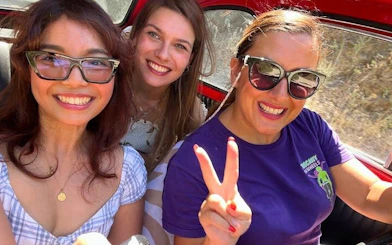 Three people smiling inside a vintage Fiat 500 during a Chianti and San Gimignano tour.