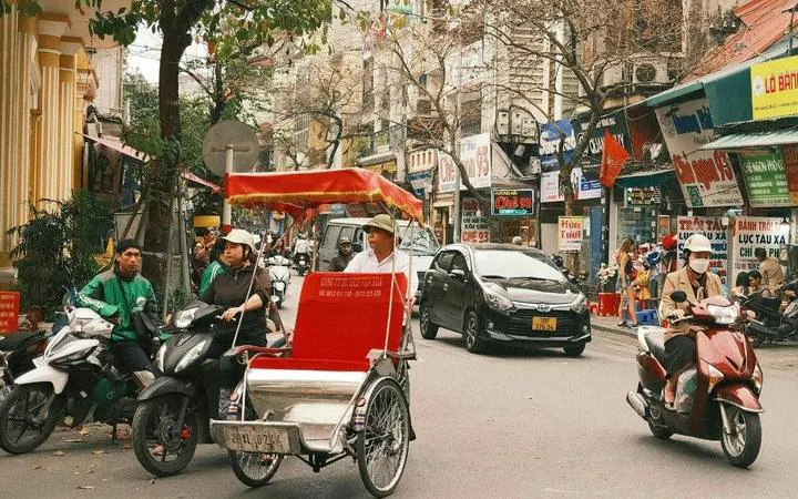 Cyclo navigating Hanoi's Old Quarter with bustling street scene and motorbikes.