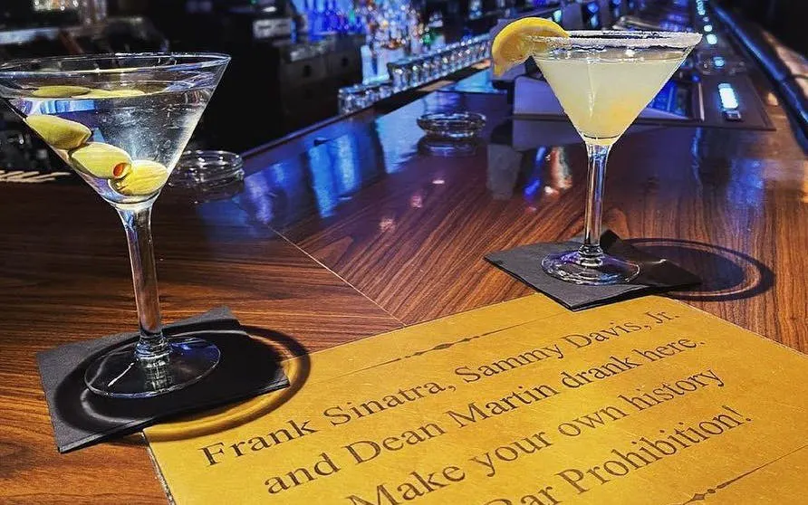 Two cocktails on a bar with a sign mentioning Frank Sinatra in Downtown Las Vegas.