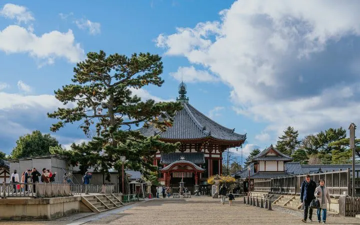Nara temple with visitors walking, surrounded by trees and traditional architecture.