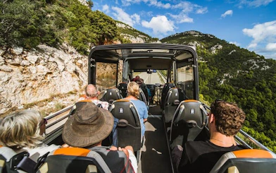 Open-top minibus on Korcula wine tour with passengers enjoying scenic hillside views.