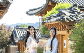 Women in traditional hanbok at a Seoul palace with Korean architecture in the background.