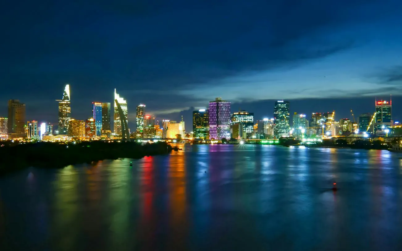 Ho Chi Minh City skyline at night with illuminated buildings reflecting on the river.