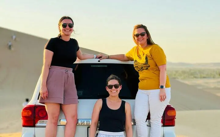Three people posing by a 4x4 vehicle in Abu Dhabi desert during a safari tour.