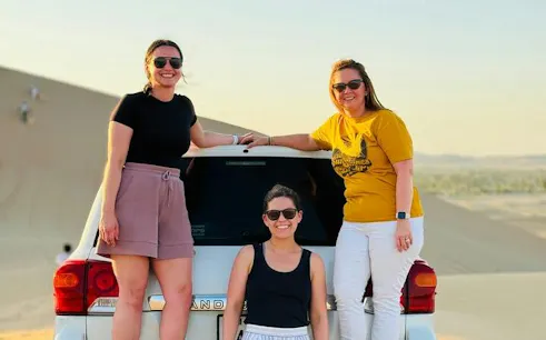 Three people posing by a 4x4 vehicle in Abu Dhabi desert during a safari tour.