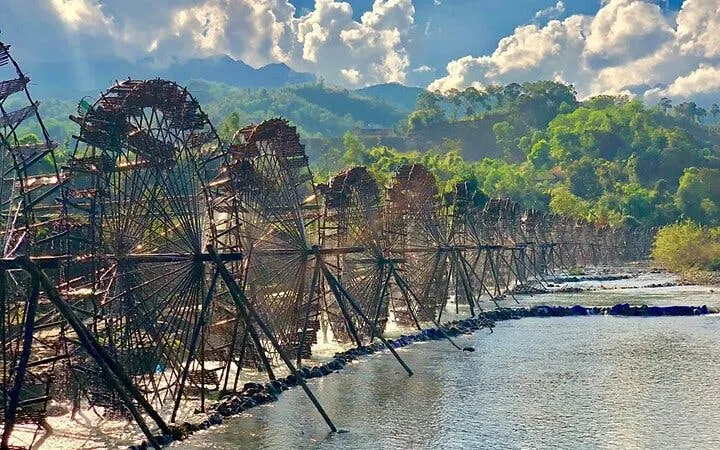 Waterwheels along a river in Sapa, Vietnam, with lush green hills in the background.
