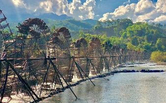 Waterwheels along a river in Sapa, Vietnam, with lush green hills in the background.