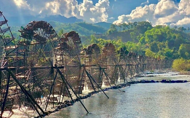 Waterwheels along a river in Sapa, Vietnam, with lush green hills in the background.