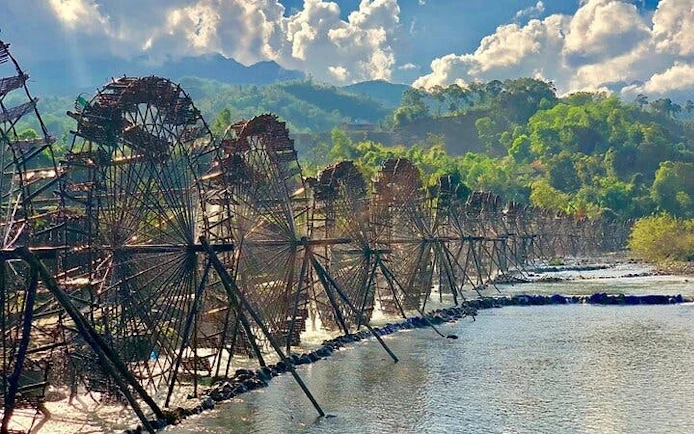 Waterwheels along a river in Sapa, Vietnam, with lush green hills in the background.