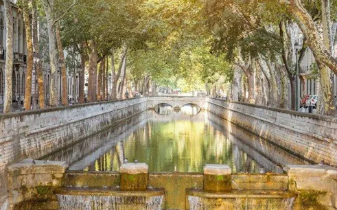 Tree-lined canal in Nîmes with stone bridge, part of self-guided audio walking tour from Arles.