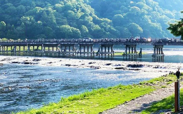Togetsukyo Bridge over Katsura River in Arashiyama, Kyoto, surrounded by lush green hills.