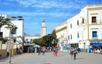Essaouira square with people walking, historic buildings, and a mosque tower in the background.