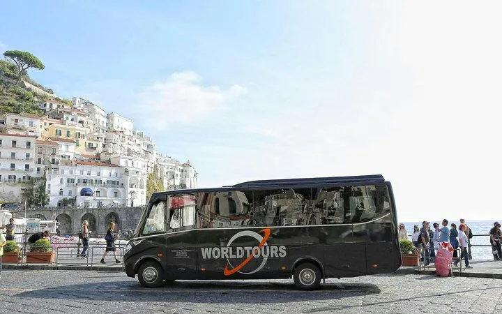 Tour bus in Amalfi with coastal buildings and sea view.