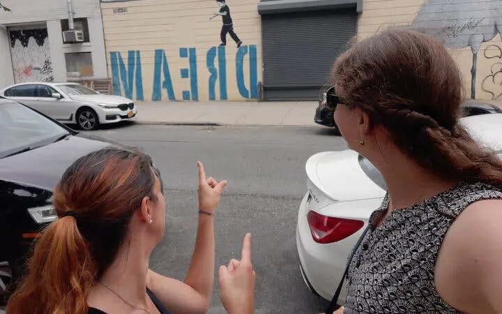 Two people pointing at street art mural with "DREAM" in Brooklyn.