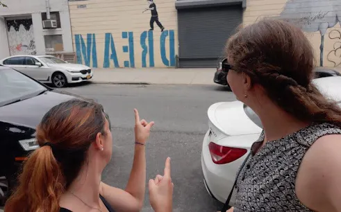 Two people pointing at street art mural with "DREAM" in Brooklyn.