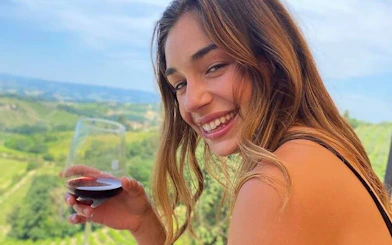 Woman enjoying wine with Tuscan vineyard view during San Gimignano tour.