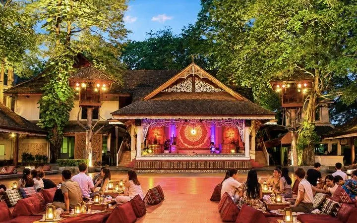 Khantoke dinner setup with guests seated on cushions, facing a lit stage at Khum Khantoke, Chiang Mai.